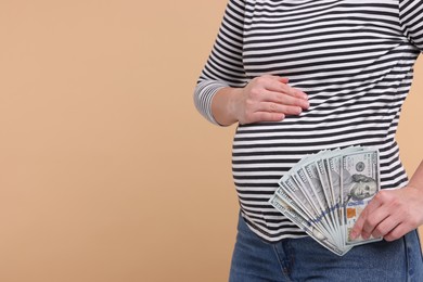 Photo of Surrogate mother. Pregnant woman with dollar banknotes on beige background, closeup. Space for text