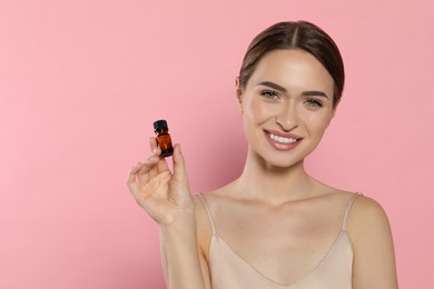 Photo of Young woman with bottle of essential oil on pink background, space for text
