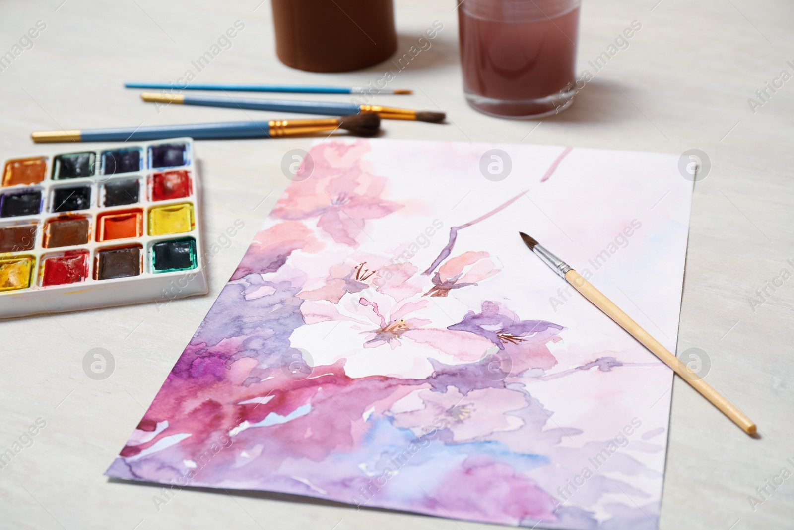 Photo of Beautiful floral picture, brushes and watercolor paints on light table