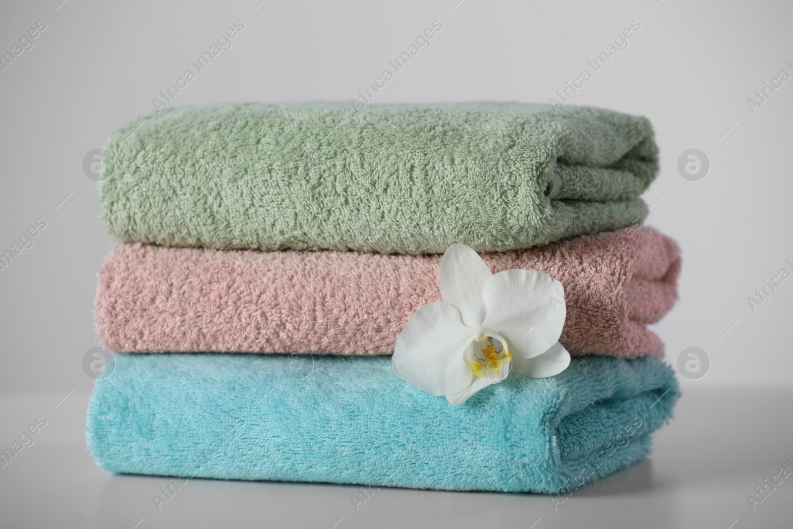 Photo of Stacked soft colorful towels with flower on white table