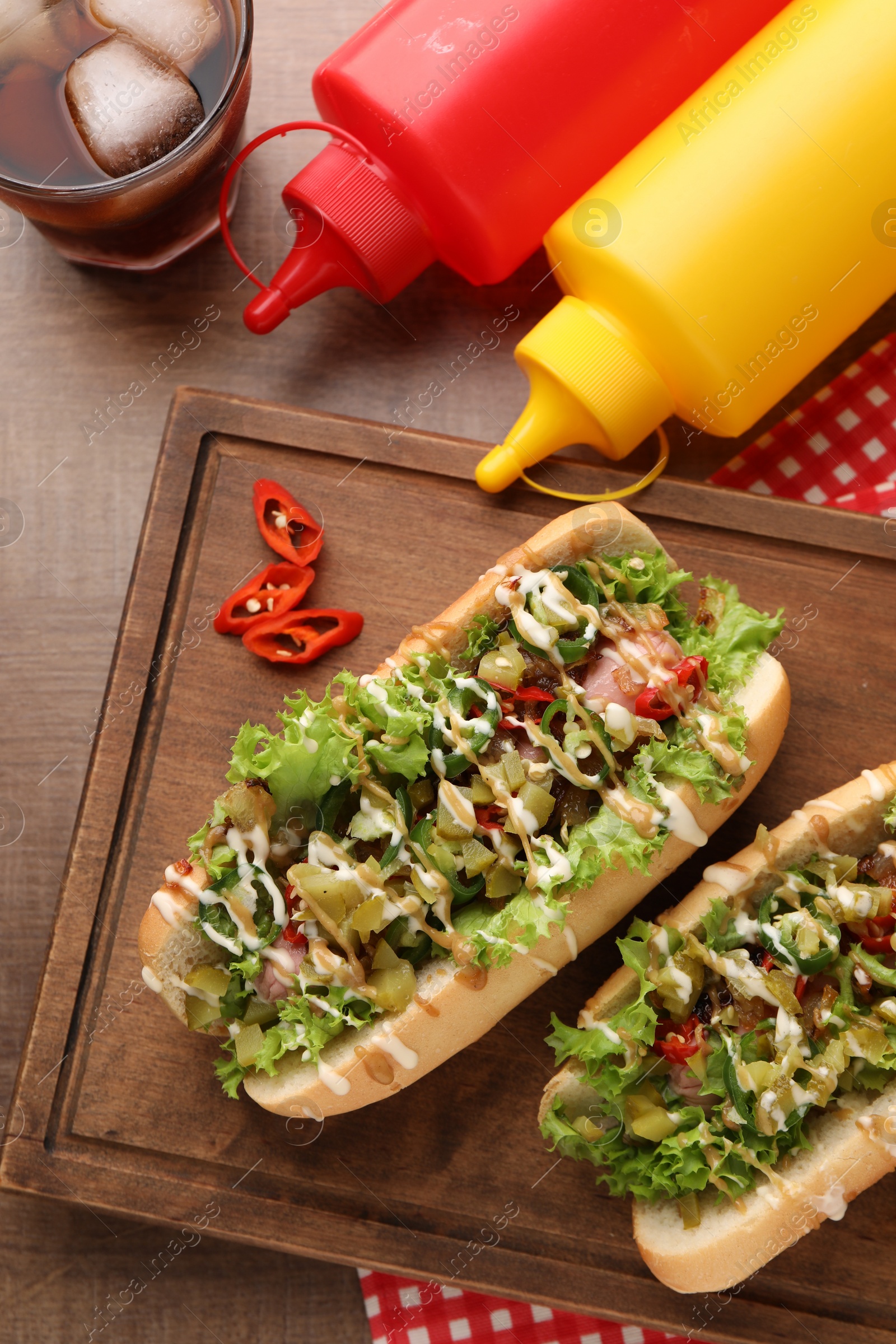 Photo of Tasty hot dogs with chili, lettuce, pickles and sauces served on wooden table, flat lay