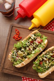 Photo of Tasty hot dogs with chili, lettuce, pickles and sauces served on wooden table, flat lay