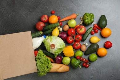 Flat lay composition with overturned paper bag and groceries on grey table