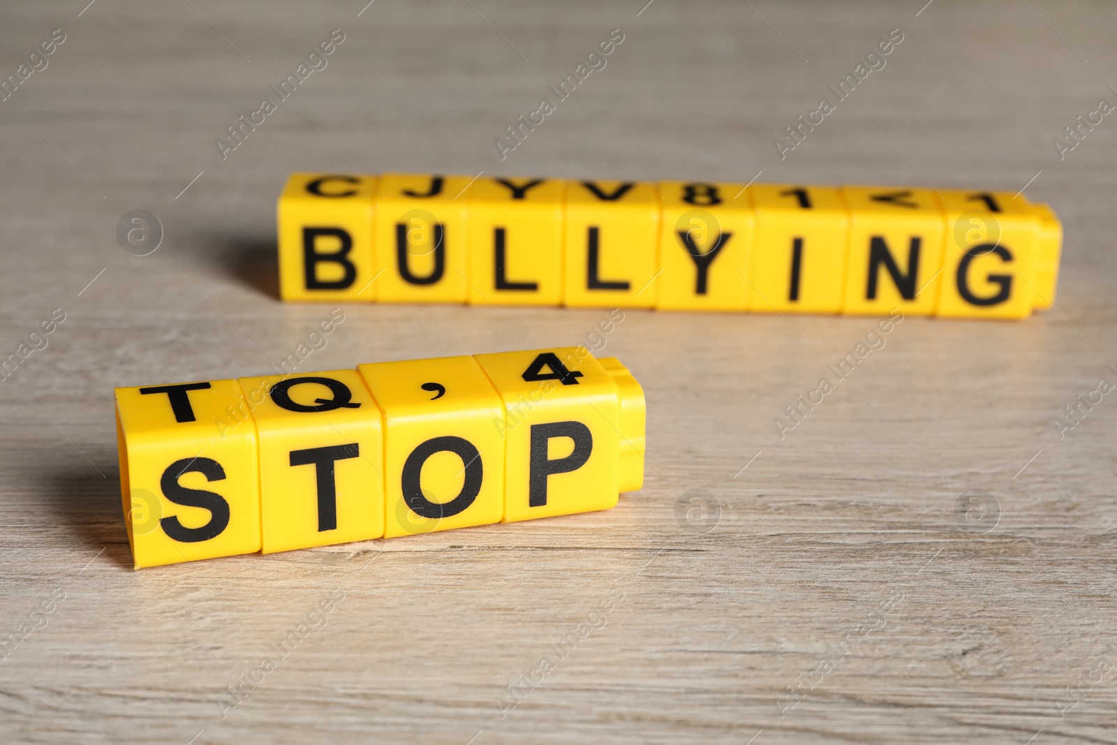 Photo of Phrase Stop Bullying made of yellow cubes with letters on wooden table, closeup