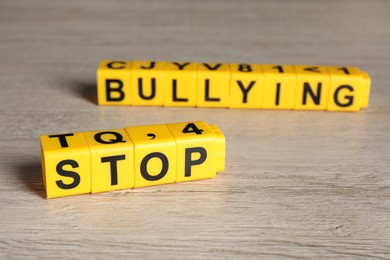 Photo of Phrase Stop Bullying made of yellow cubes with letters on wooden table, closeup