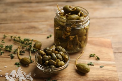 Photo of Tasty capers, thyme and salt on wooden table