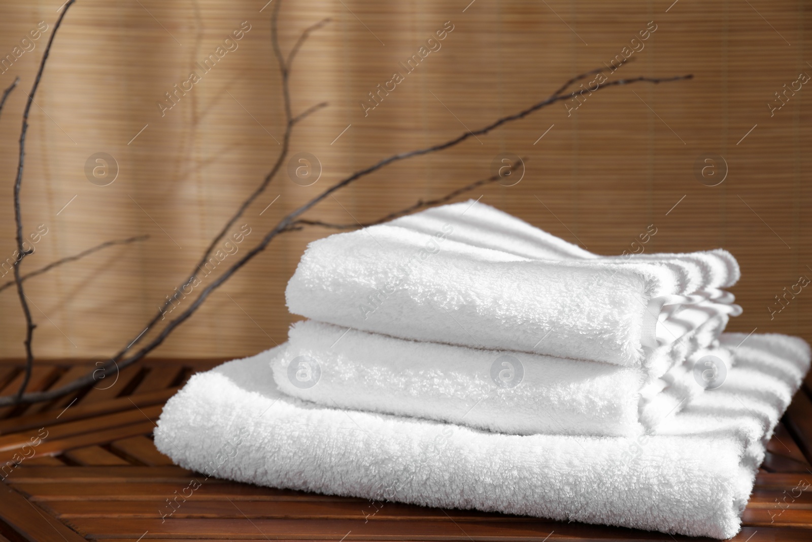 Photo of Stacked soft towels on wooden table and tree branches indoors