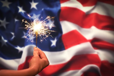 Image of 4th of July - Independence Day of USA. Woman holding burning sparkler against American flag, closeup