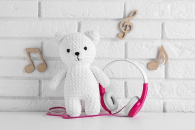 Photo of Baby songs. Toy bear and headphones on white wooden table and notes