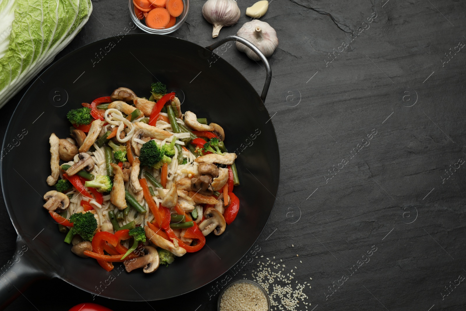 Photo of Stir fried noodles with mushrooms, chicken and vegetables in wok on black table, flat lay. Space for text