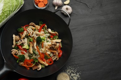 Stir fried noodles with mushrooms, chicken and vegetables in wok on black table, flat lay. Space for text