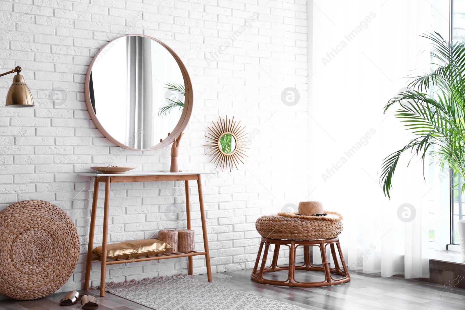 Photo of Hallway interior with big round mirror, table and decor near brick wall