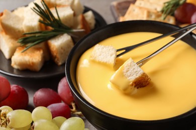 Photo of Tasty cheese fondue, forks with bread pieces and snacks on table, closeup
