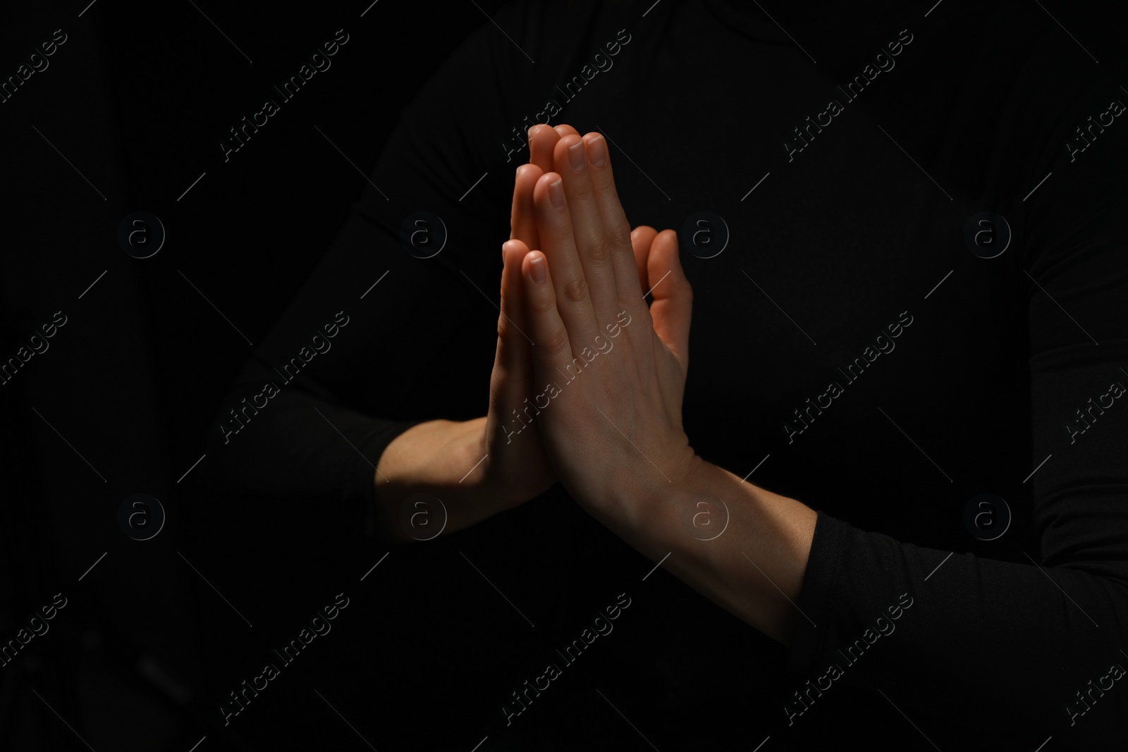 Photo of Religion. Christian woman praying on black background, closeup