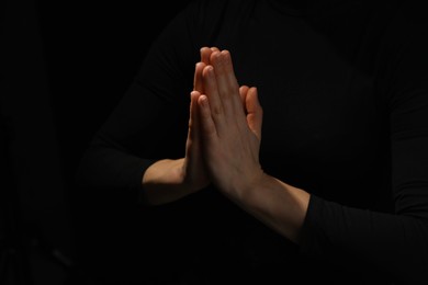 Religion. Christian woman praying on black background, closeup