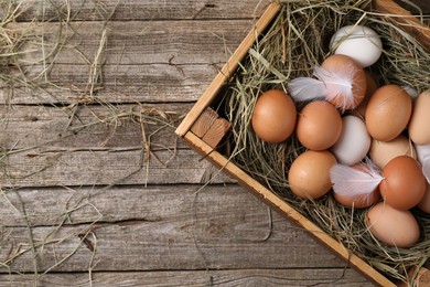 Fresh chicken eggs and dried hay in crate on wooden table, top view. Space for text