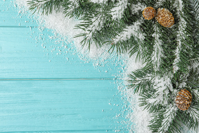 Photo of Top view of fir branches and snow on light blue wooden background, space for text. Winter holidays