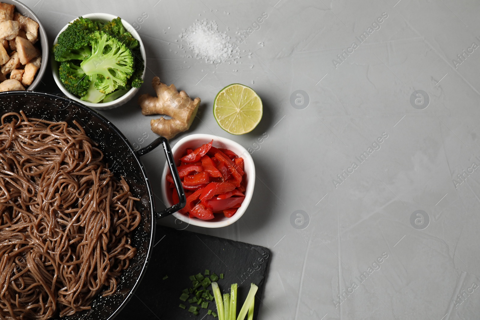 Photo of Wok with noodles, chicken and other products on light grey table, flat lay. Space for text