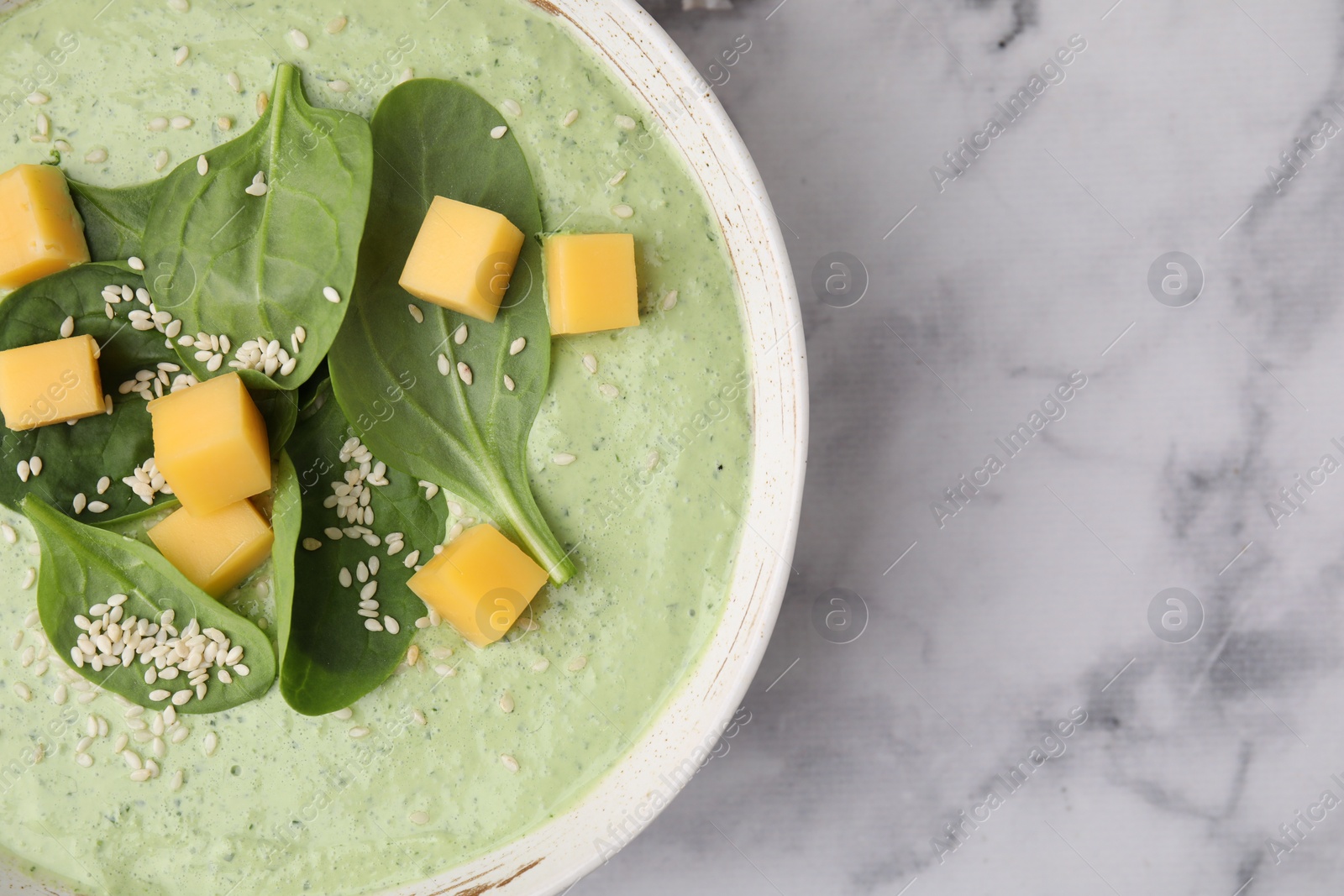 Photo of Delicious spinach cream soup with cheese and sesame seeds in bowl on white marble table, top view. Space for text