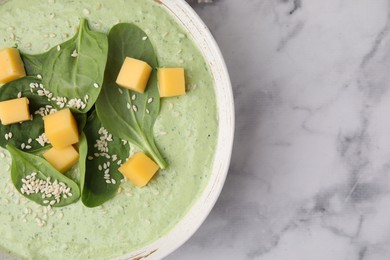 Delicious spinach cream soup with cheese and sesame seeds in bowl on white marble table, top view. Space for text