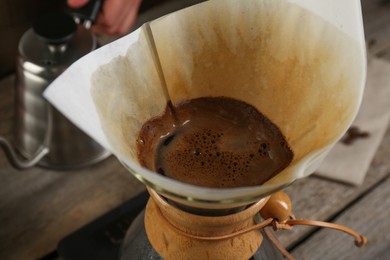 Photo of Brewing aromatic coffee in glass chemex coffeemaker with paper filter on table, closeup