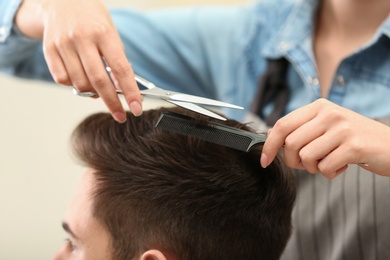 Barber making stylish haircut with professional scissors in beauty salon, closeup