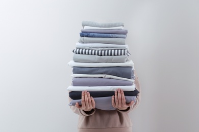 Woman holding stack of clean bed linens on light grey background