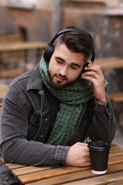 Handsome man in warm scarf with paper cup listening to music in outdoor cafe