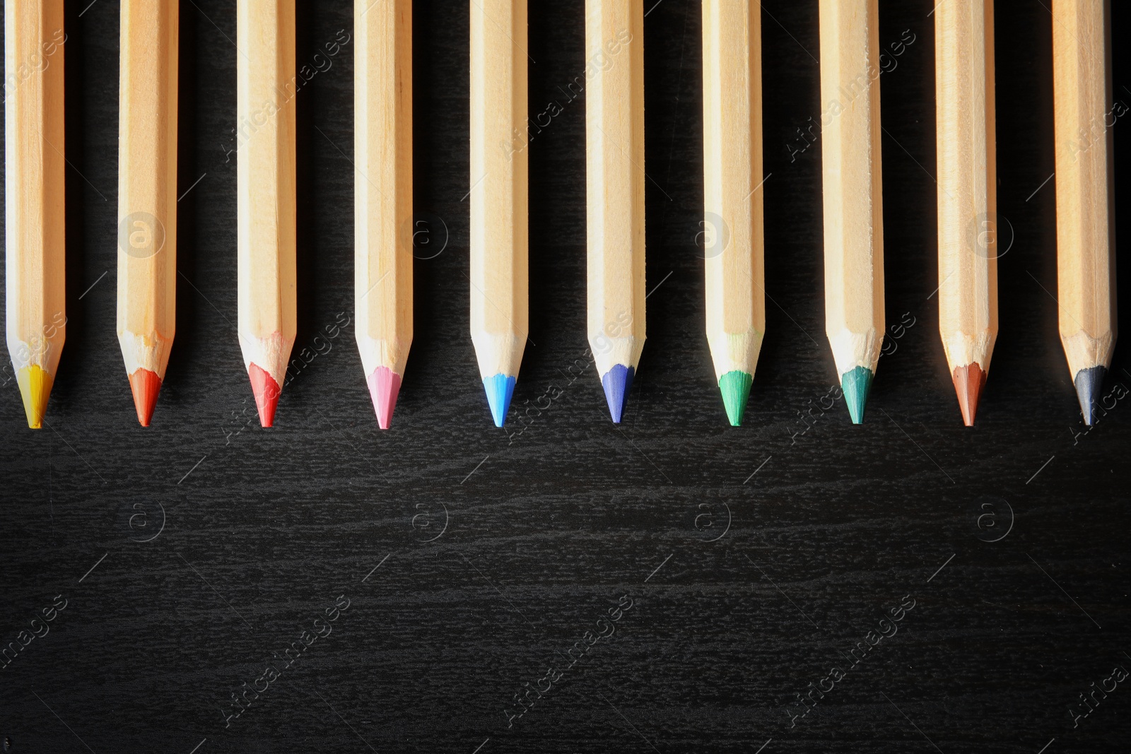 Photo of Pencils of different colors with space for design on wooden background, top view. School stationery