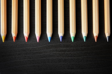 Photo of Pencils of different colors with space for design on wooden background, top view. School stationery