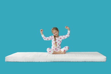 Little girl waking up on mattress against light blue background