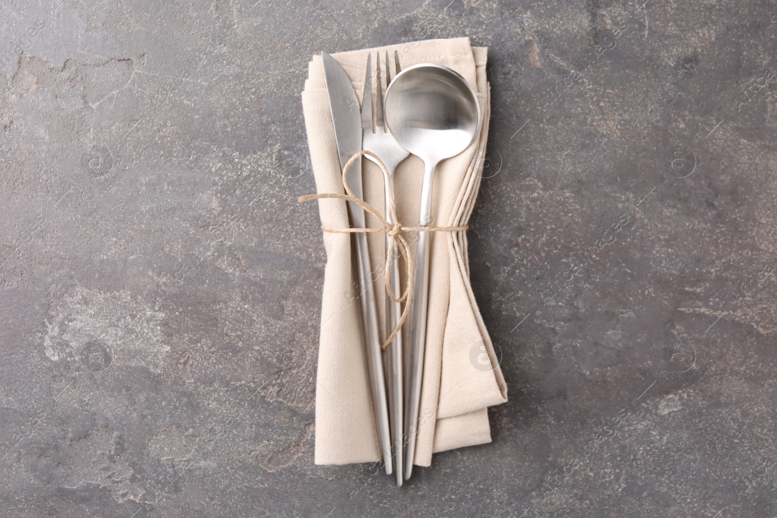 Photo of Set of stylish cutlery and napkin on grey textured table, top view