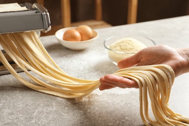 Young woman preparing noodles with pasta maker at table