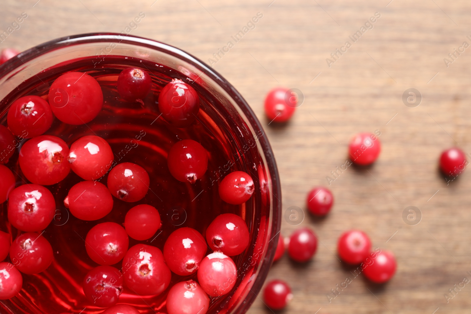 Photo of Tasty cranberry juice in glass and fresh berries on wooden table, top view. Space for text