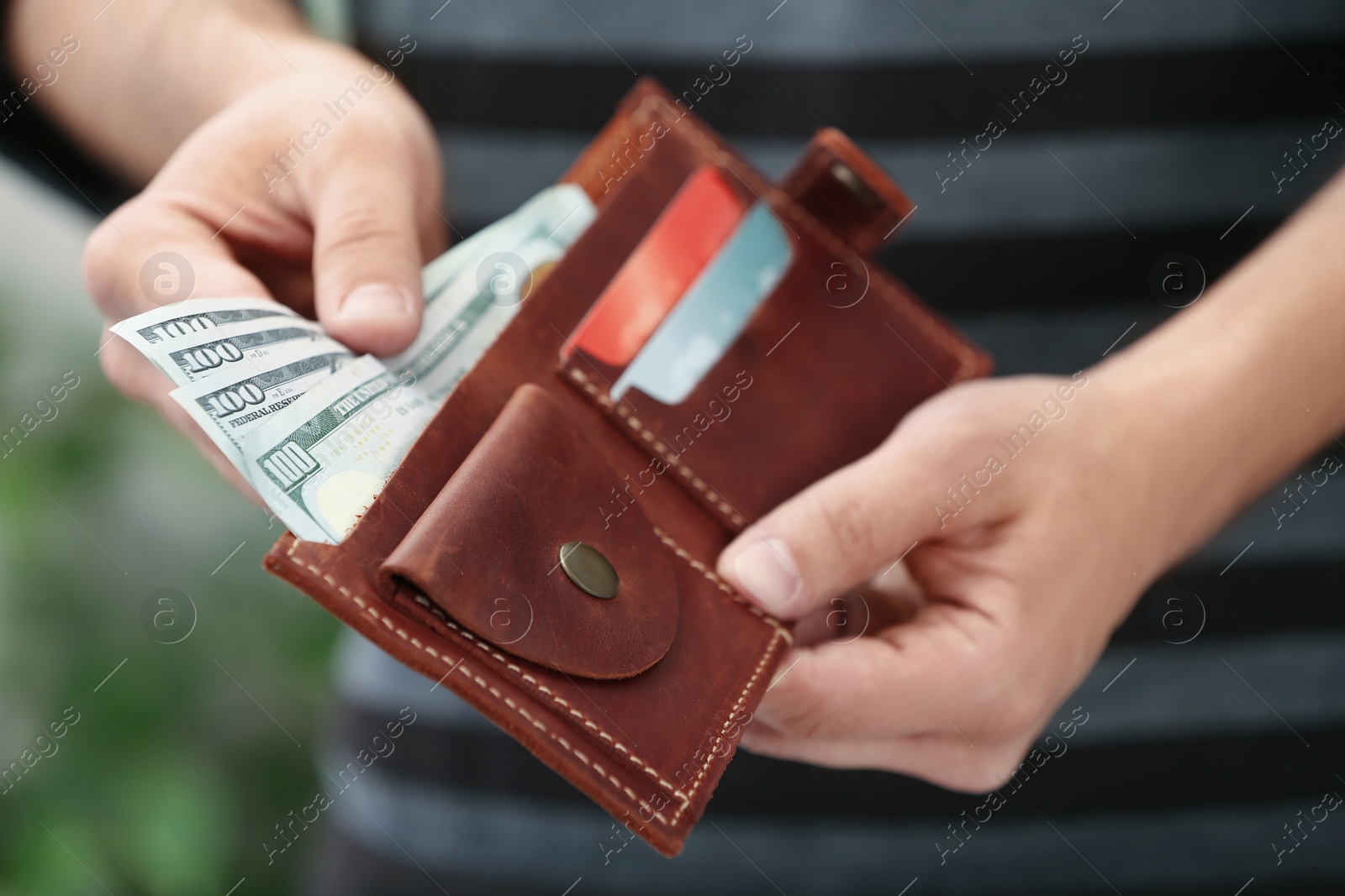 Photo of Man putting money into wallet on blurred background, closeup