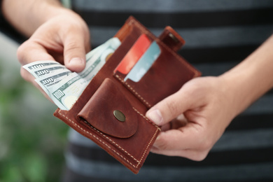 Man putting money into wallet on blurred background, closeup