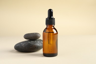 Bottle of cosmetic serum and stones on beige background