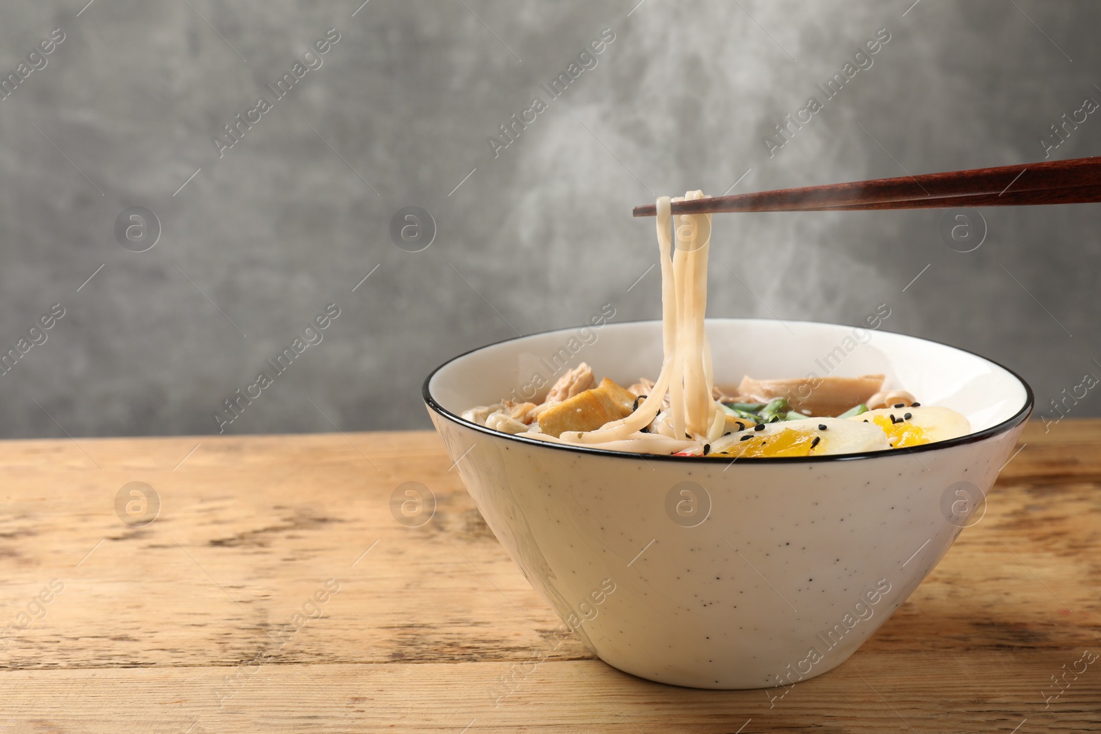 Image of Noodle soup. Eating hot ramen with chopsticks at wooden table, closeup. Space for text