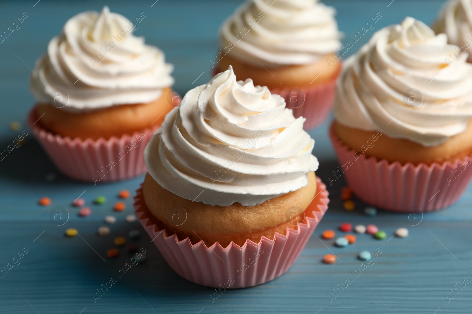 Photo of Delicious cupcakes decorated with cream on light blue wooden table, closeup