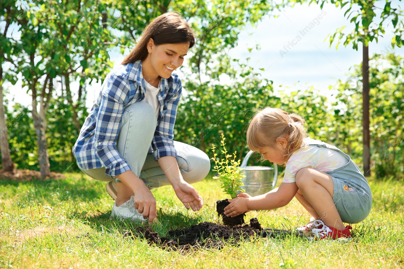 Photo of Mother and her daughter planting tree together in garden