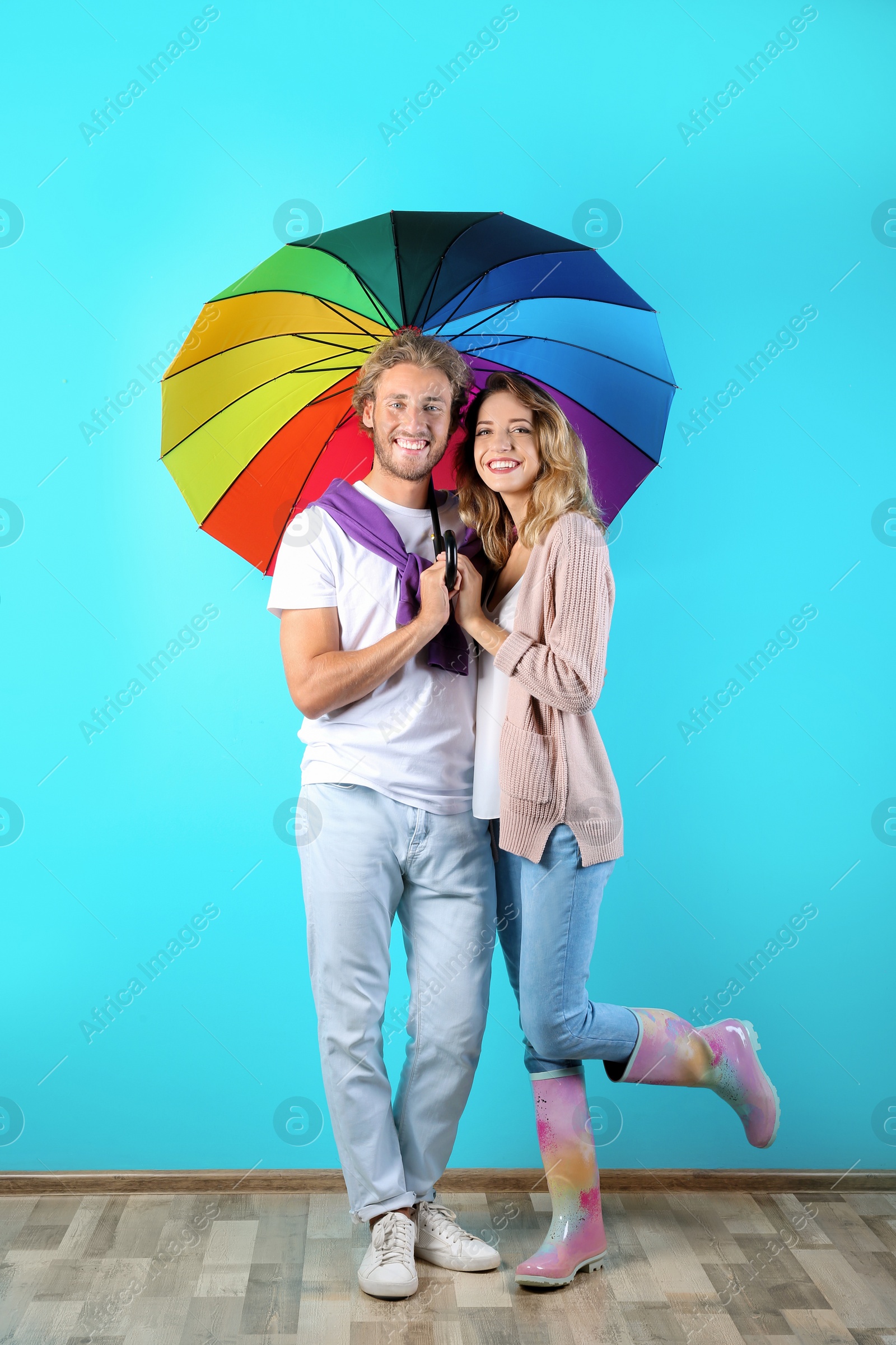 Photo of Couple with rainbow umbrella near color wall