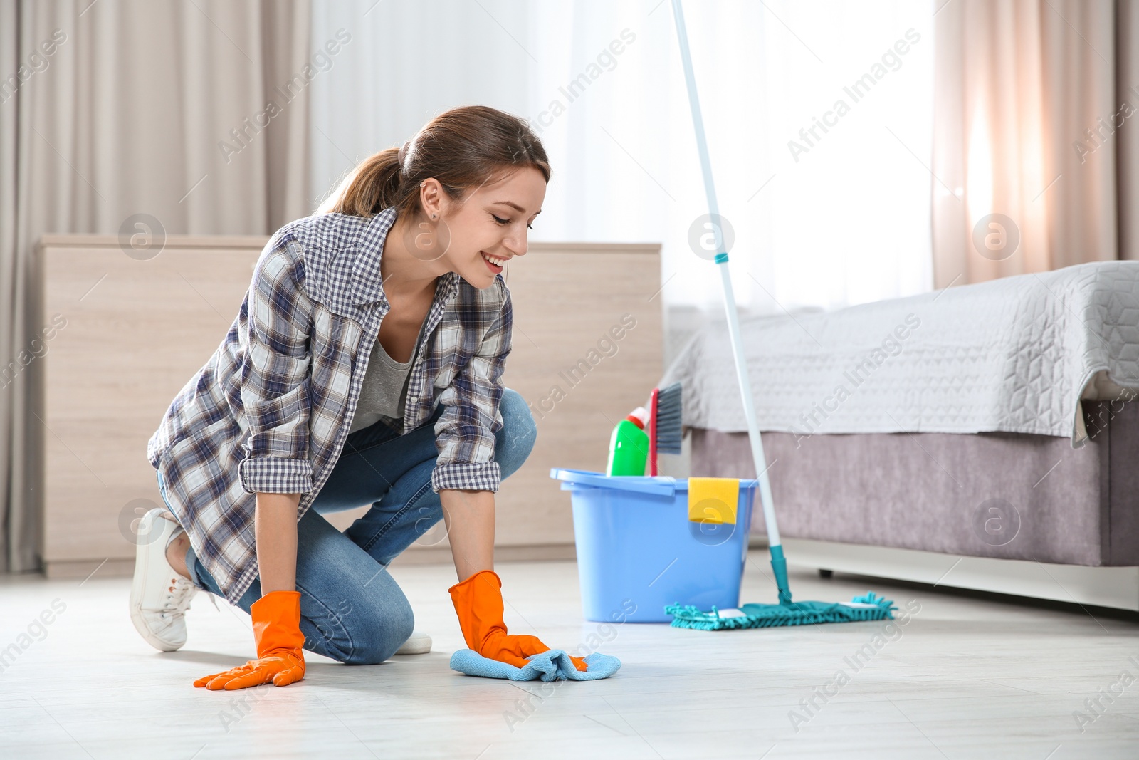 Photo of Young woman washing floor with rag and detergent in bedroom. Cleaning service