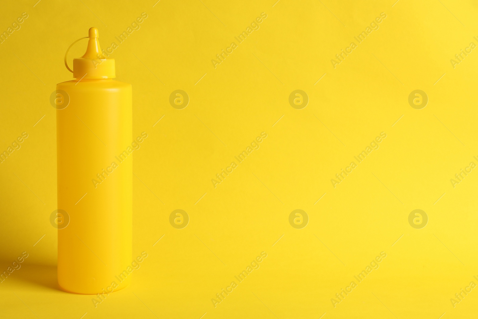 Photo of Spicy mustard in plastic bottle on yellow background, space for text
