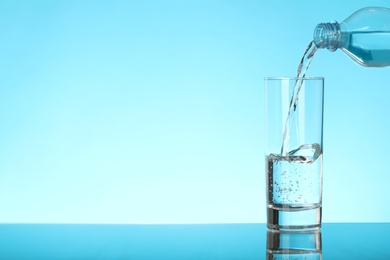 Pouring water from bottle into glass on blue background, space for text. Refreshing drink