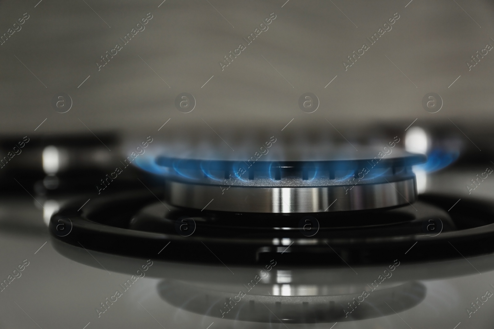 Photo of Gas burner with blue flame on modern stove, closeup