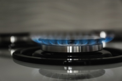 Photo of Gas burner with blue flame on modern stove, closeup