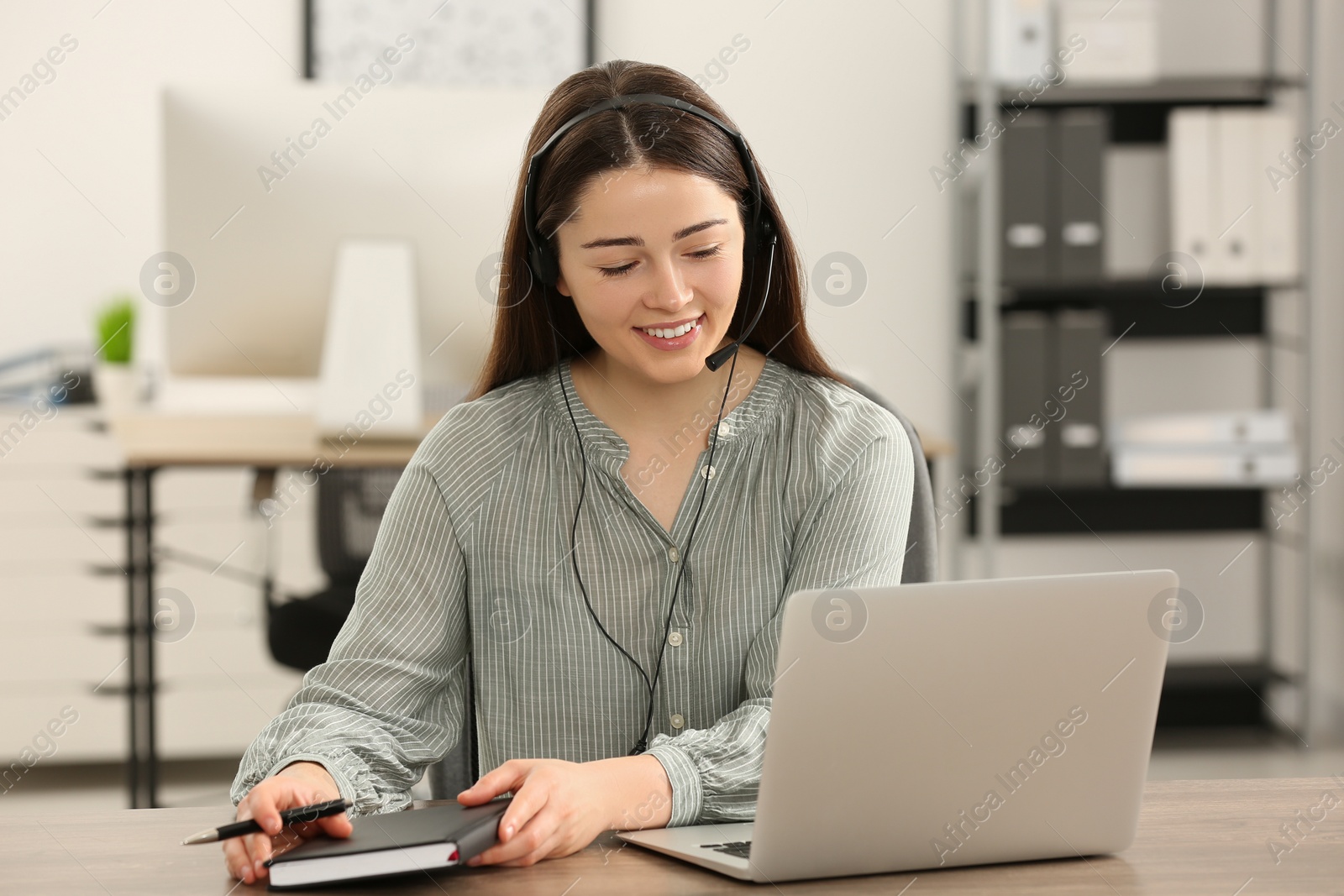 Photo of Hotline operator with headset and notebook working in office