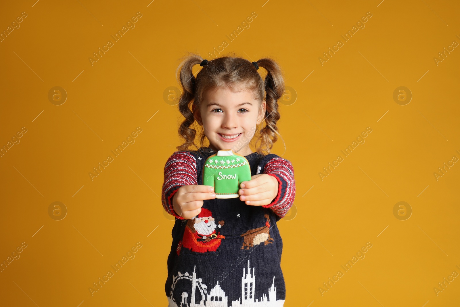 Photo of Cute little girl with Christmas gingerbread cookie on yellow background