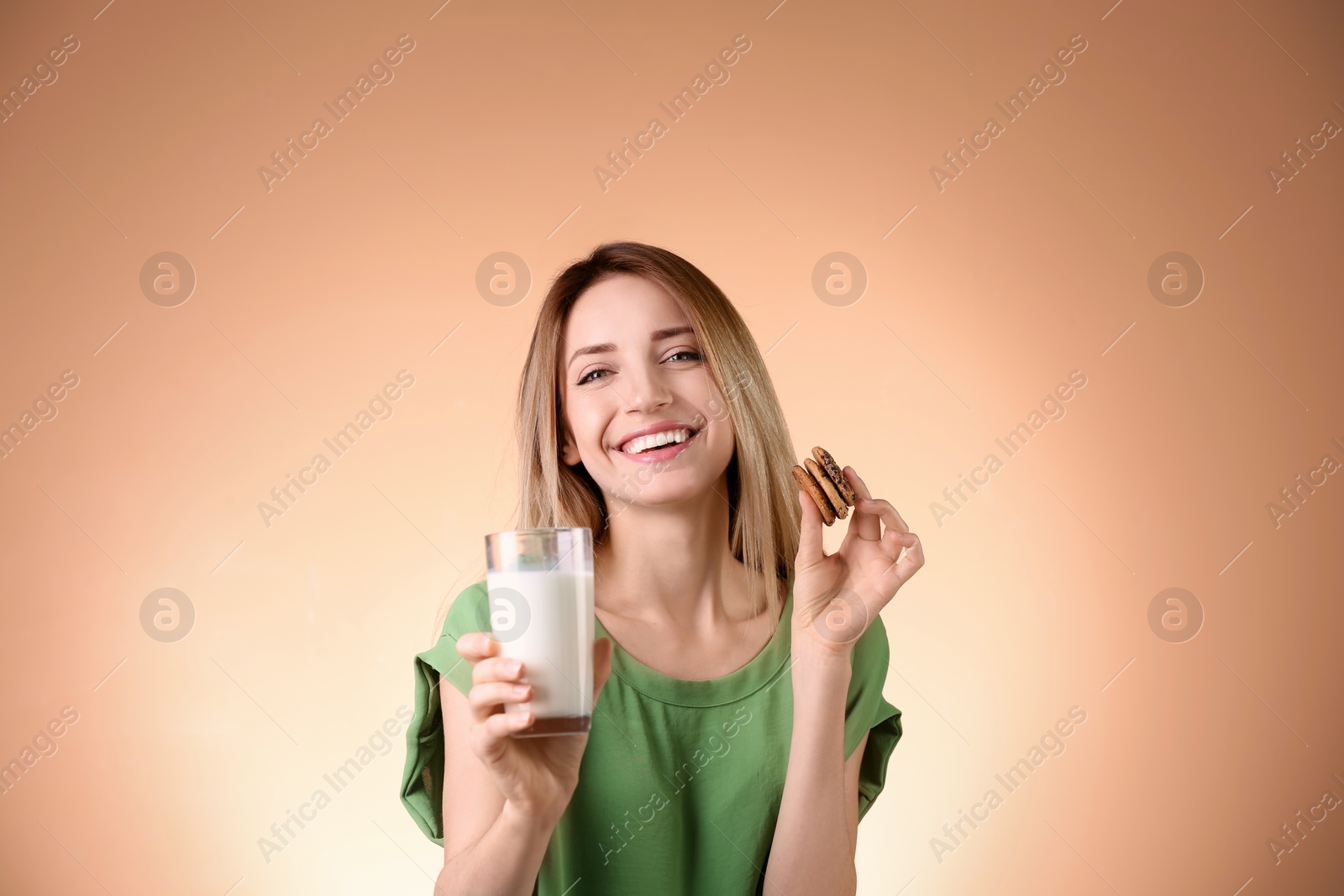 Photo of Beautiful young woman drinking milk with cookies on color background