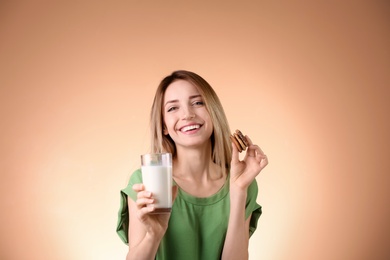 Beautiful young woman drinking milk with cookies on color background